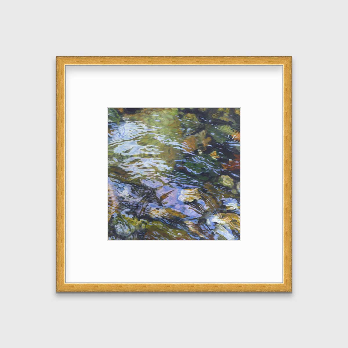 A green, brown and beige abstract river rock in water print in a gold frame with a mat hangs on a white wall.