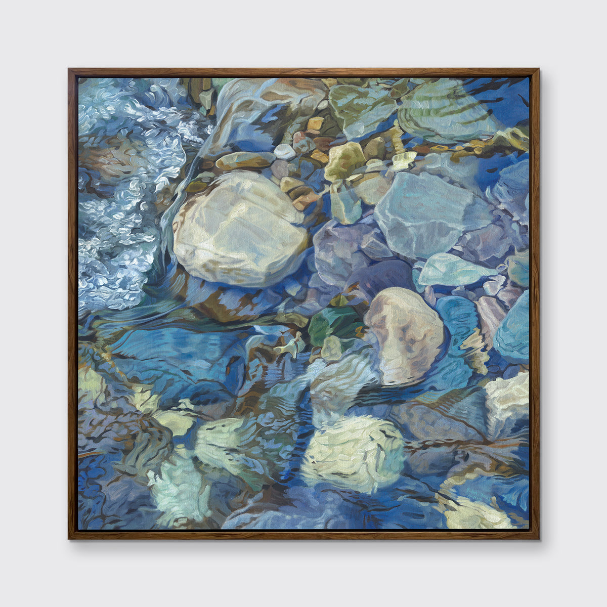 Abstracted print of grey, brown, green and blue river rocks under water hangs in an oak wood floater frame on a white wall.