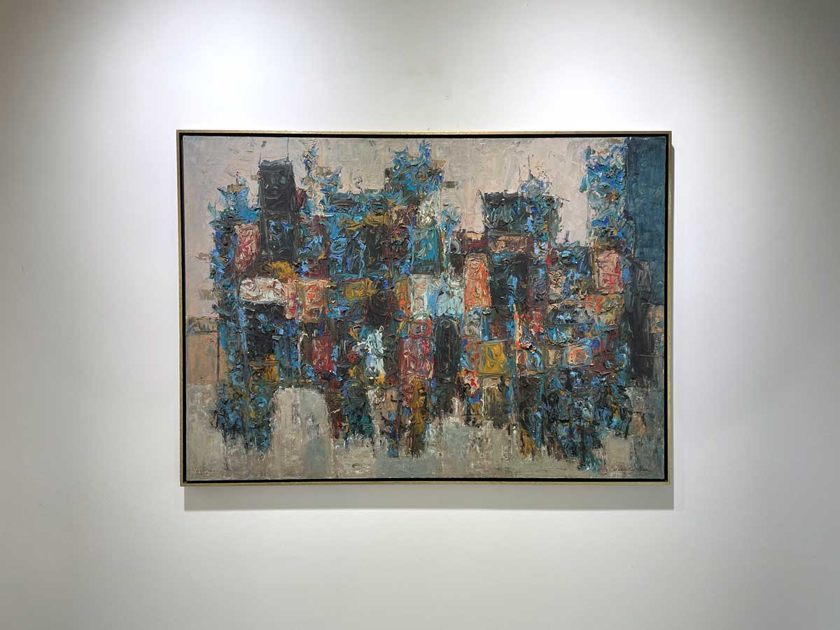 A multicolored abstract painting in a warm gold floater frame hangs on a white wall.