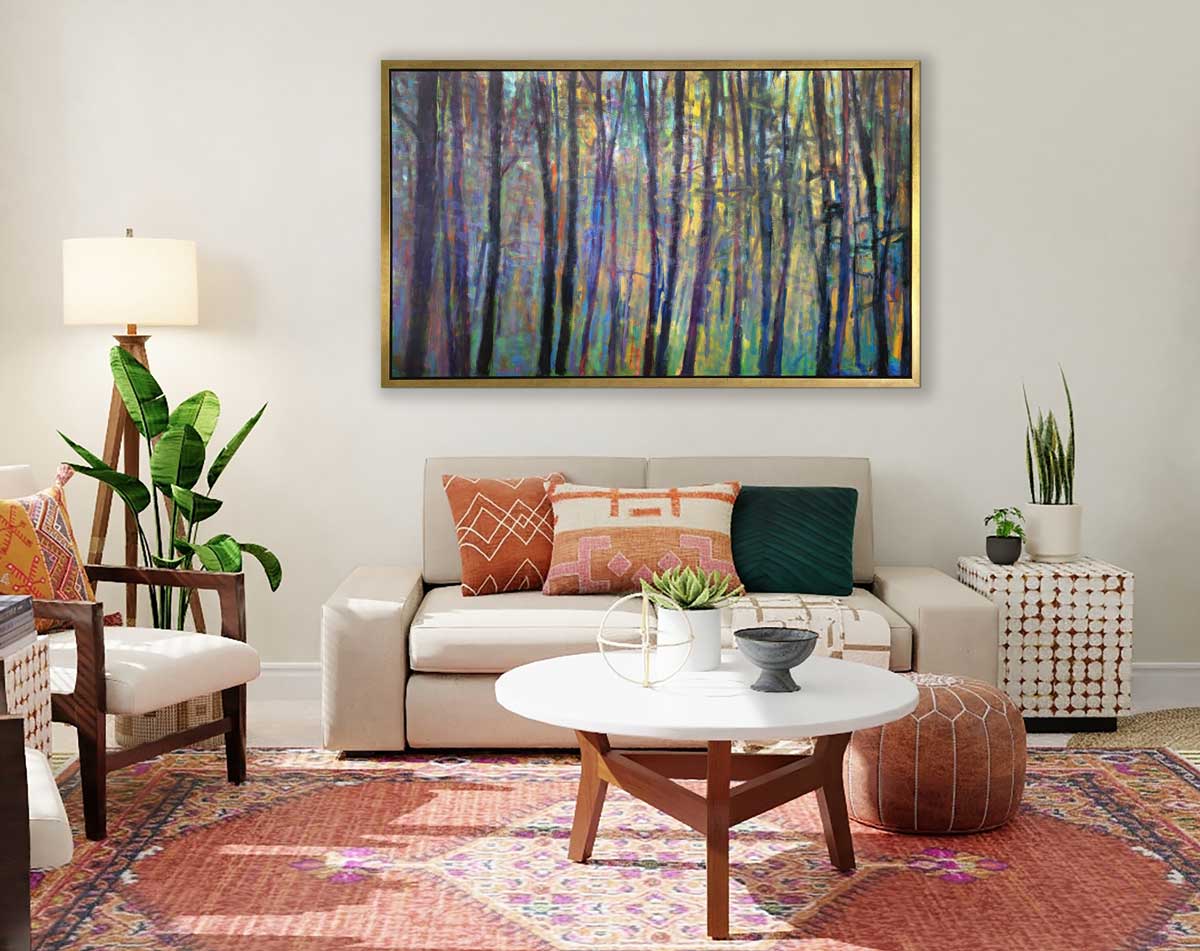 A multicolored abstract tree landscape print in a gold floater frame hangs on a white wall above a oversized white sofa with printed pillows, a white round coffee table and a white chair.