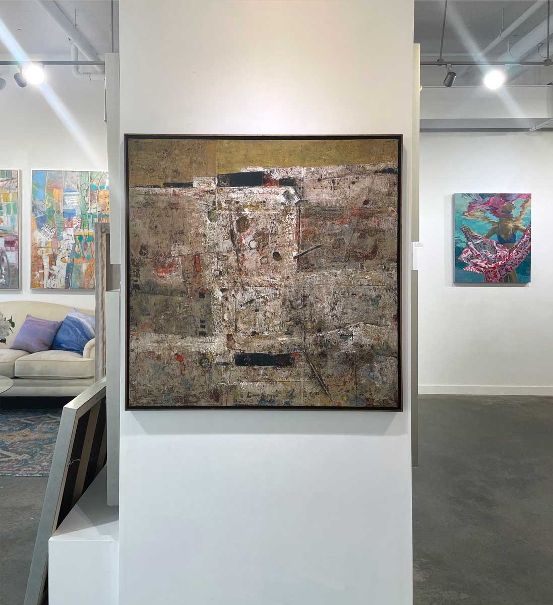 A white, grey and dark yellow abstract painting in a gold floater frame hangs on a white wall.