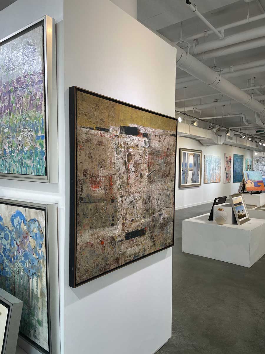A left side-angle view of a white, grey and dark yellow abstract painting in a gold floater frame hangs on a white wall.