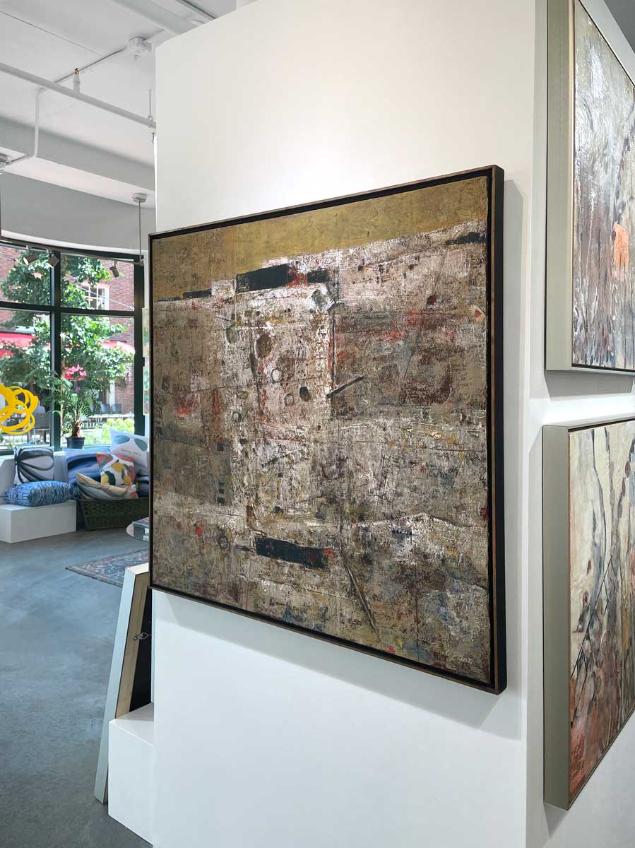 A right side-angle view of a white, grey and dark yellow abstract painting in a gold floater frame hangs on a white wall.