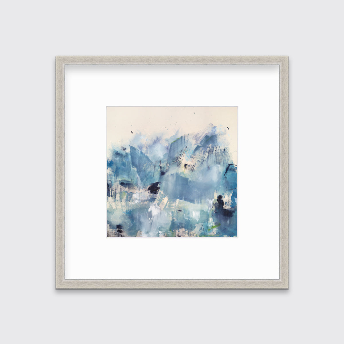 A blue and white abstract paper print framed in a silver frame hangs on a white wall.