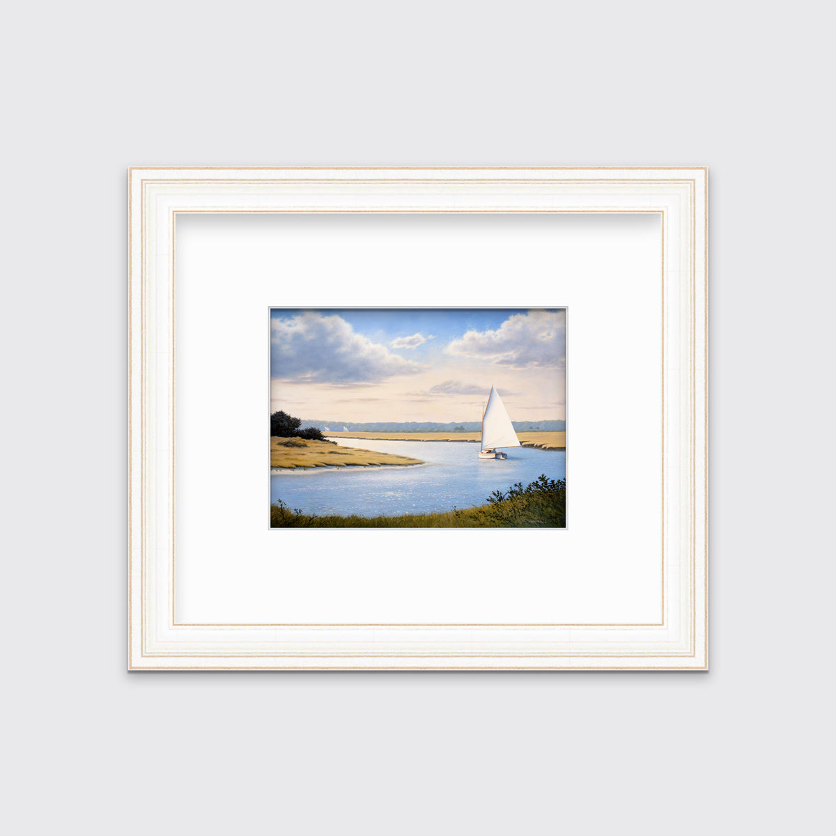 A print of a sailboat going down a winding blue river in a distressed white frame and mat hangs on a white wall.