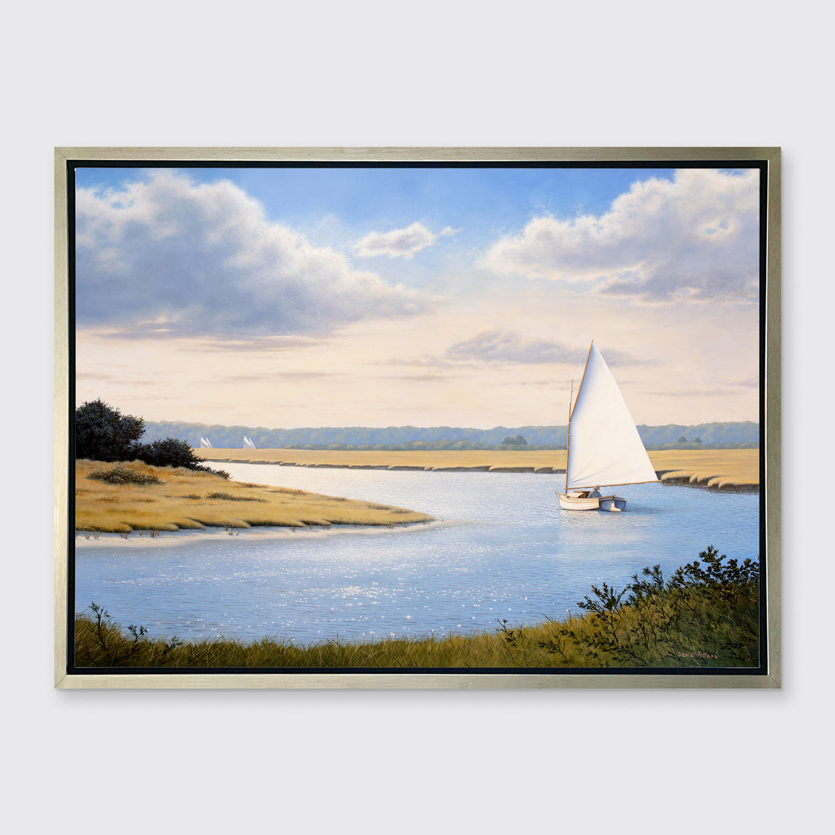 A print of a sailboat going down a winding blue river in a silver floater frame hangs on a white wall.
