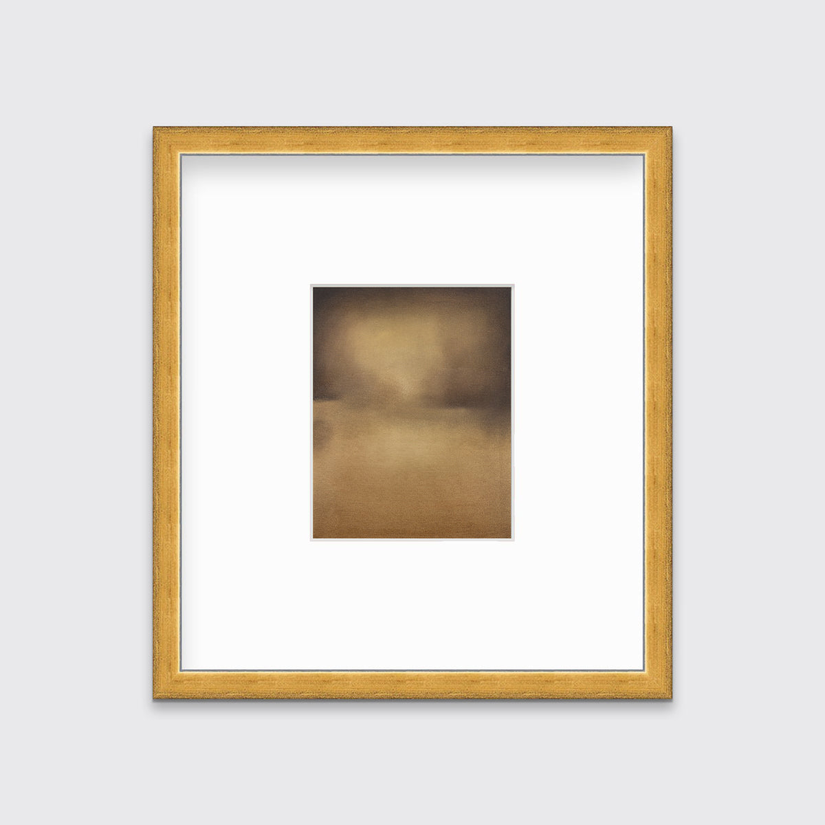 A brown and gold abstract print in a gold frame with a mat hangs on a white wall.