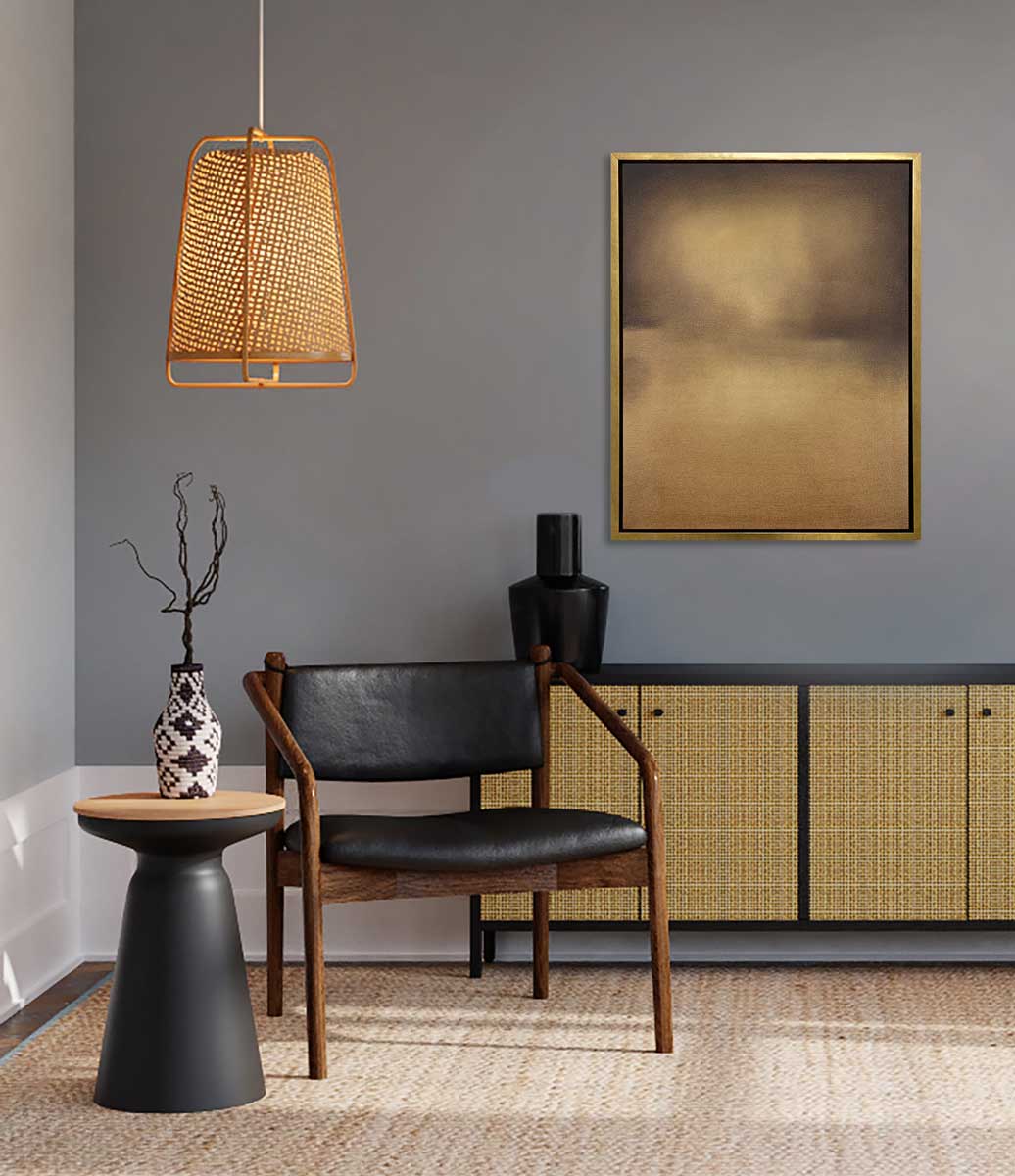 A brown and gold abstract print in a gold floater frame hangs on a grey wall above a black and rattan sideboard with a black vase, a black and dark wood chair and a black side table with a black and white vase.