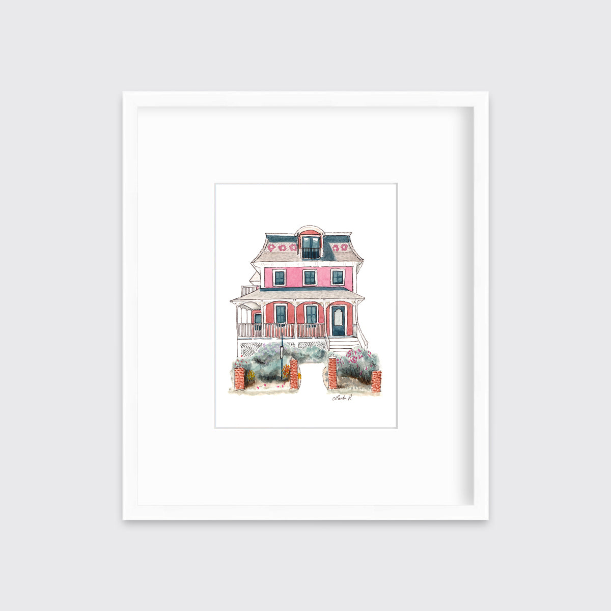 A pink and red house print in a white frame with a mat hangs on a white wall.