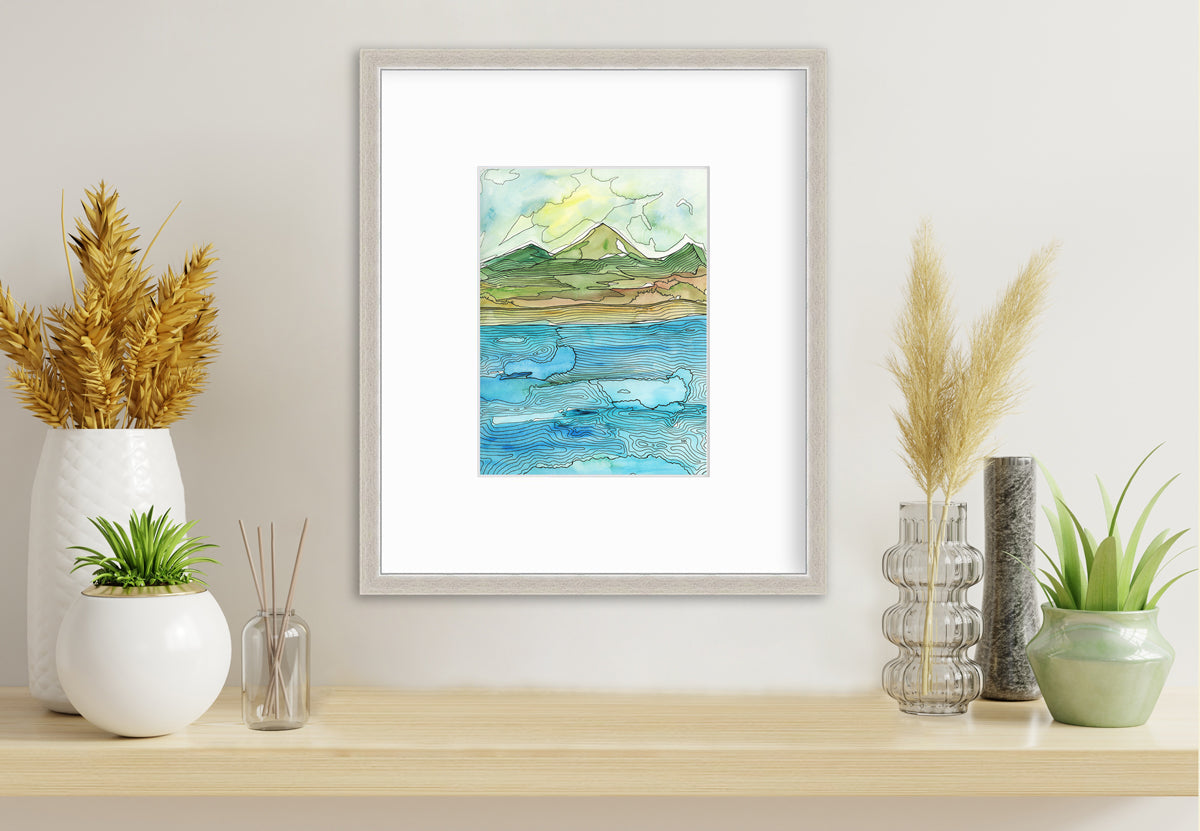 A blue, green, brown and light yellow abstract landscape with black outlines print in a silver frame with a mat hangs on a white wall above a beige surface with four various sized floral decorations.