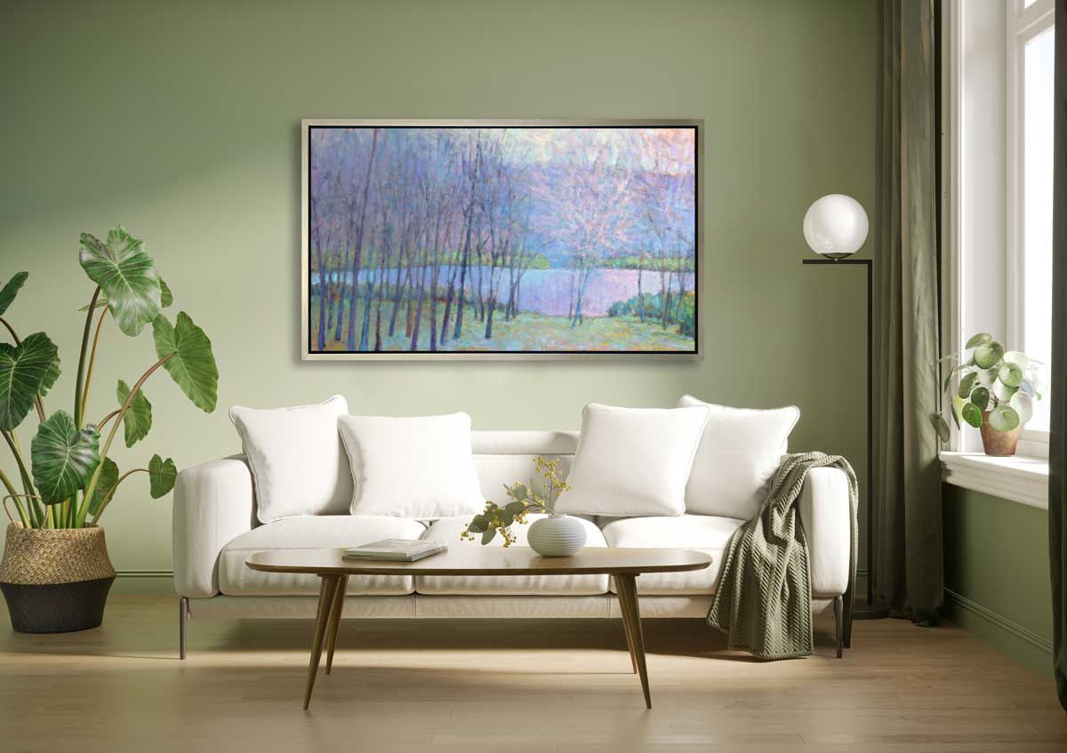 A blue, purple and green abstract landscape print in a silver floater frame hangs on a light green wall above a white sofa with pillows, a wooden coffee table and a potted floor plant.