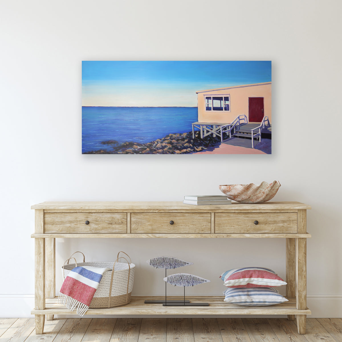 A painting of a house on the water above a console table.