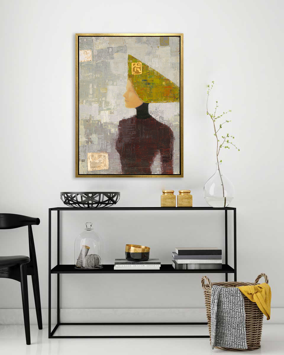 A grey, olive green and dark red abstract print of a woman with a headpiece in a gold floater frame hangs on a white wall above a black shelf with black and gold accessories.