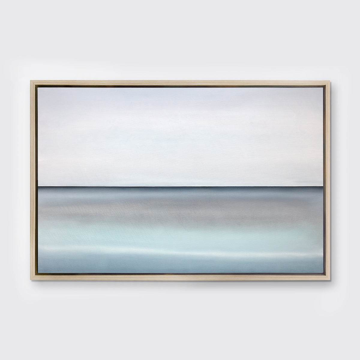 A tonal blue abstract landscape with a defined horizon print in a white oak wood floater frame hangs on a white wall.