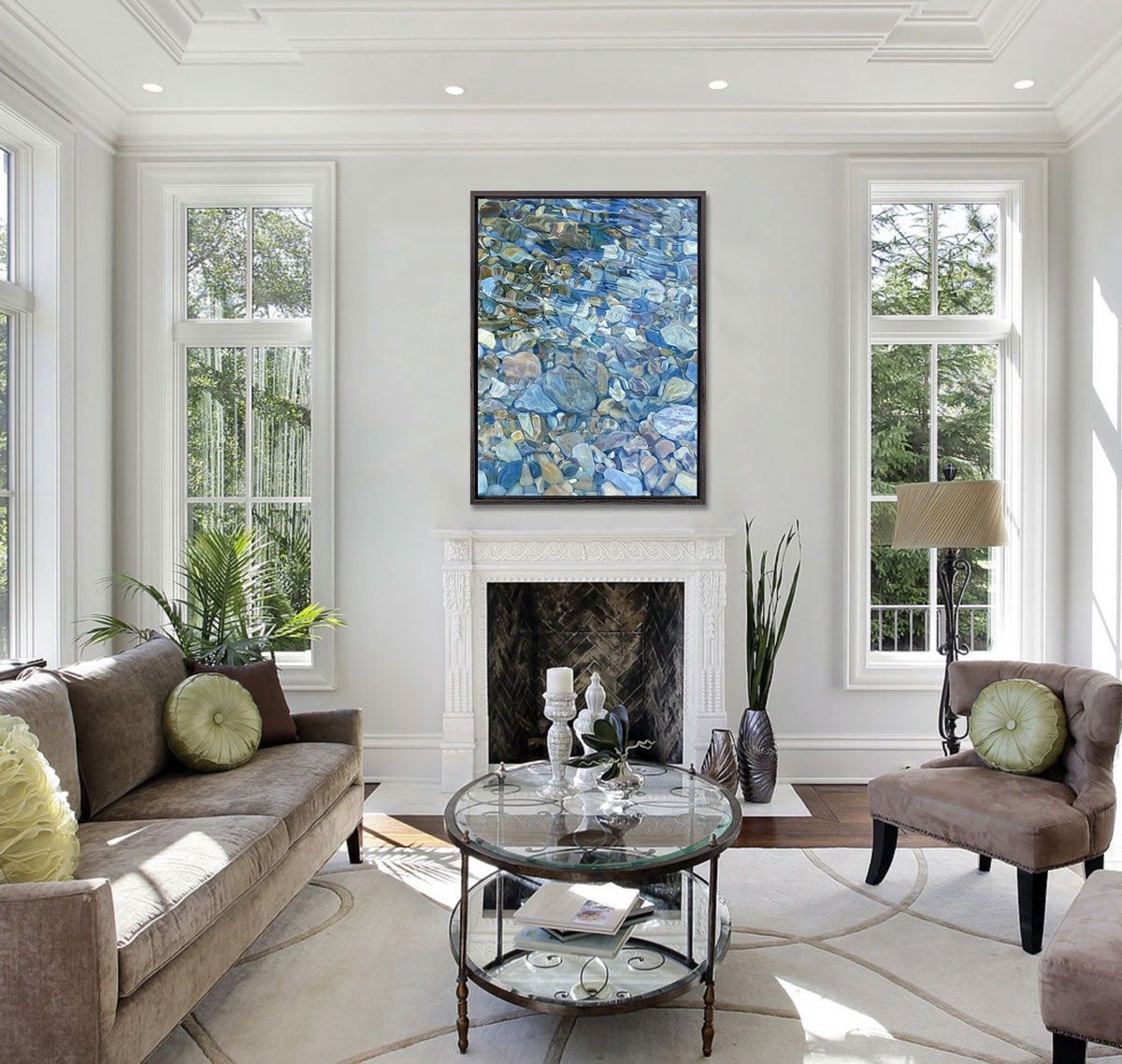 A print of rocks under water in a black floater frame above a fireplace. A brown sofa with green throw pillows face matching chairs, with a glass coffee table at the center of the room.