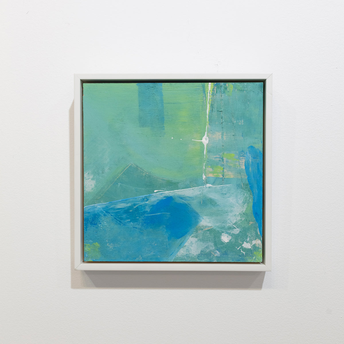 An abstract painting with blue and green patches is hung on a gallery wall. Wired and ready to hang.
