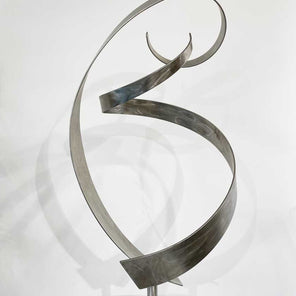 Abstract stainless steel sculpture by Joe Sorge sitting on a white pedestal in front of a white wall. 