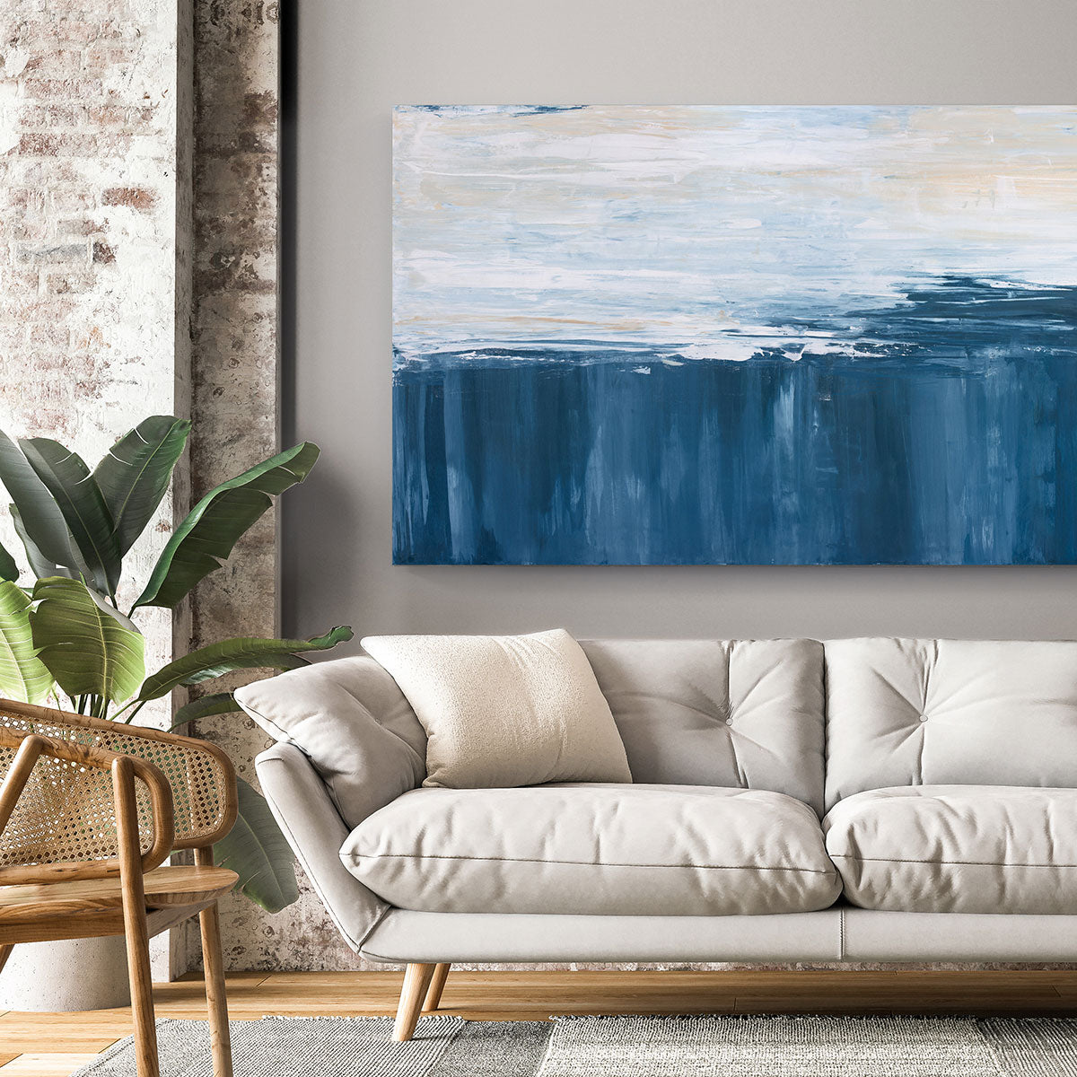 An abstract painting of blue and white forms converging is hung above a beige sofa.