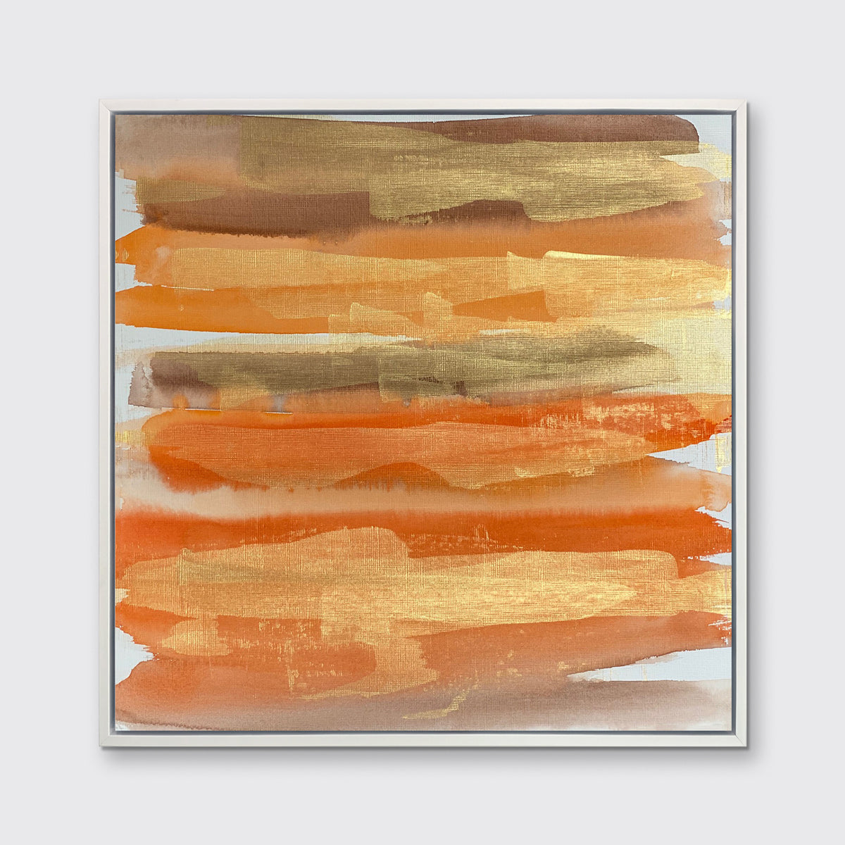 A gold, orange and light brown abstract print in a white floater frame hangs on a white wall.