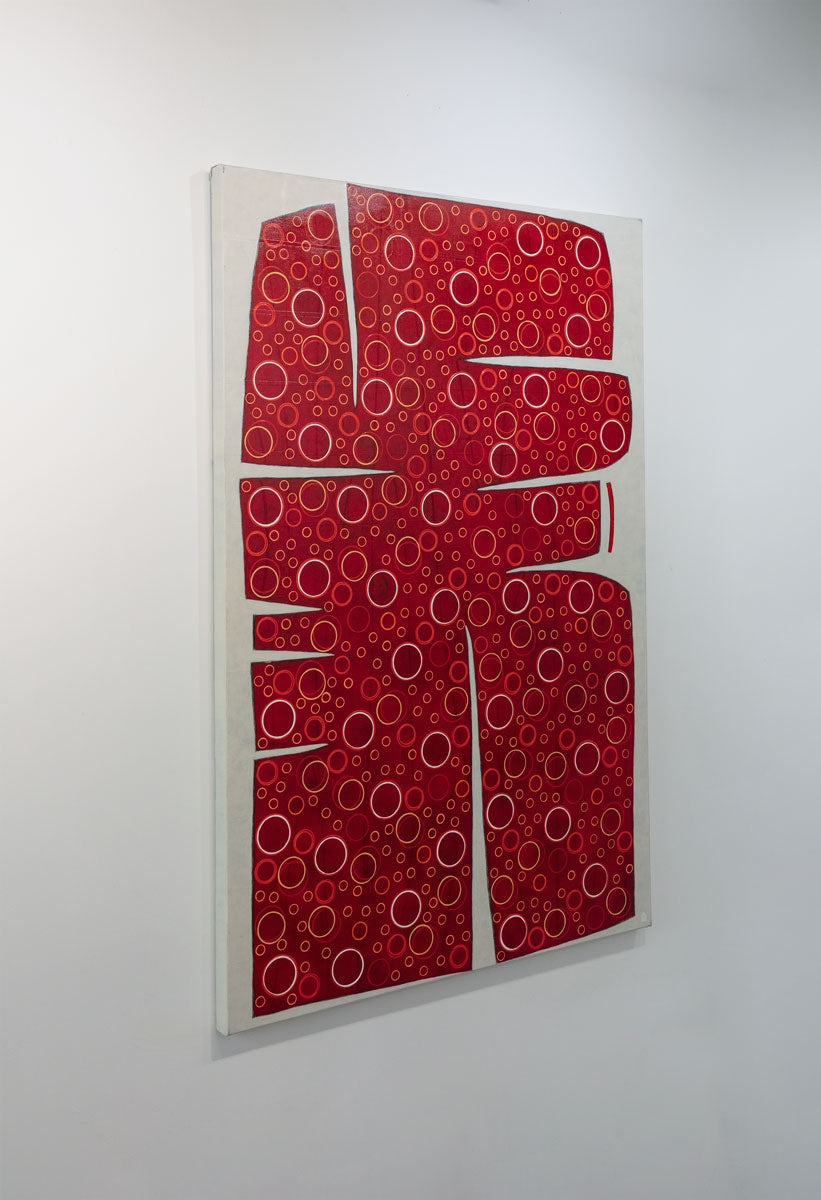 A large abstract painting of an irregular red form containing yellow and white circles is seen at an angle on a gallery wall.