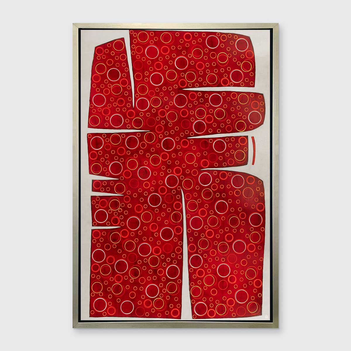 A red, yellow and white abstract print in a silver floater frame hangs on a white wall.