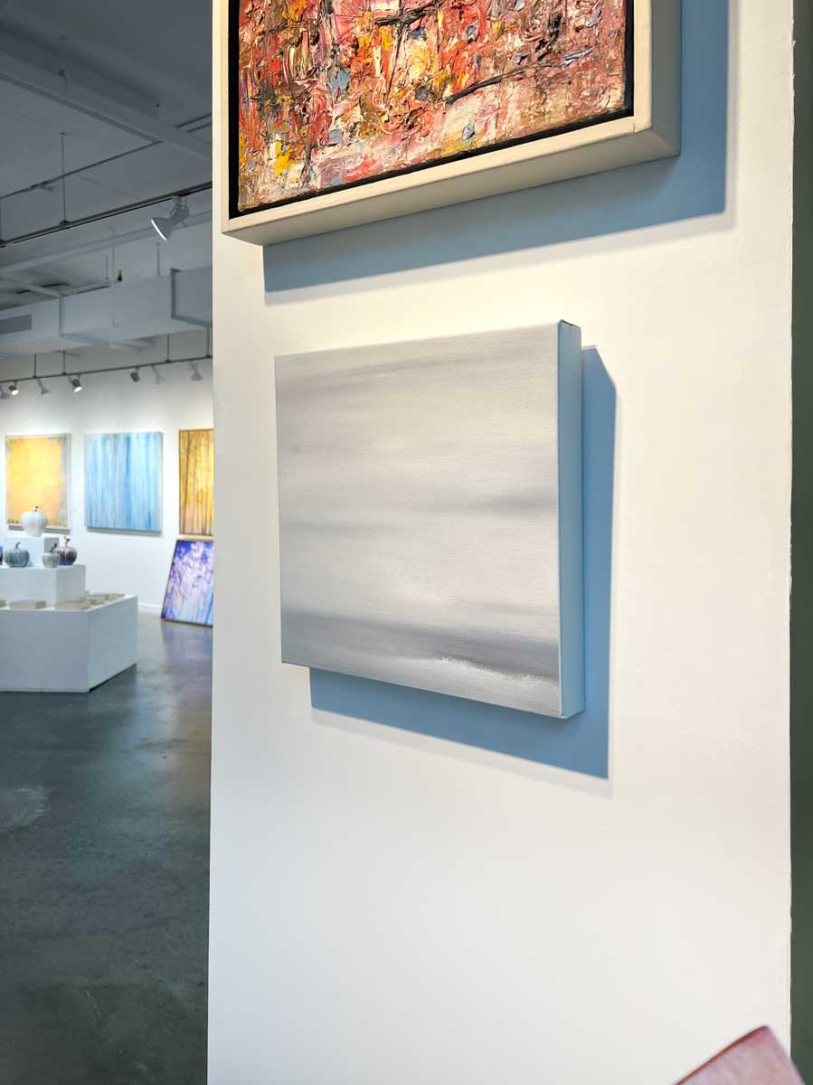 A right side-angle view of a tonal grey abstract painting by Tony Iadicicco hangs on a white wall.