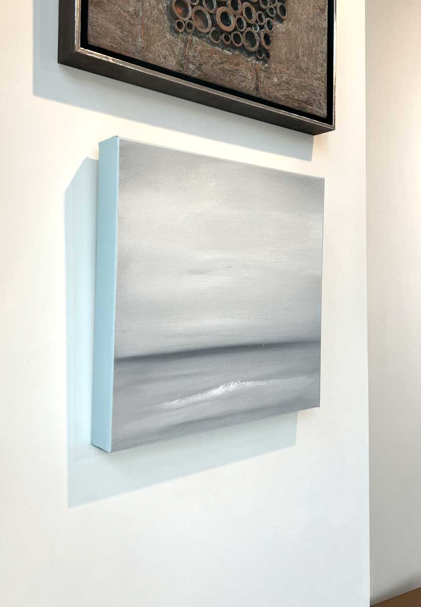 A left side-angle view of a tonal grey and white abstract painting by Tony Iadicicco hangs on a white wall.