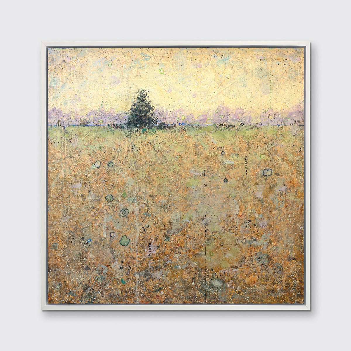 A yellow and green abstract landscape with a tree print in a white floater frame hangs on a white wall.