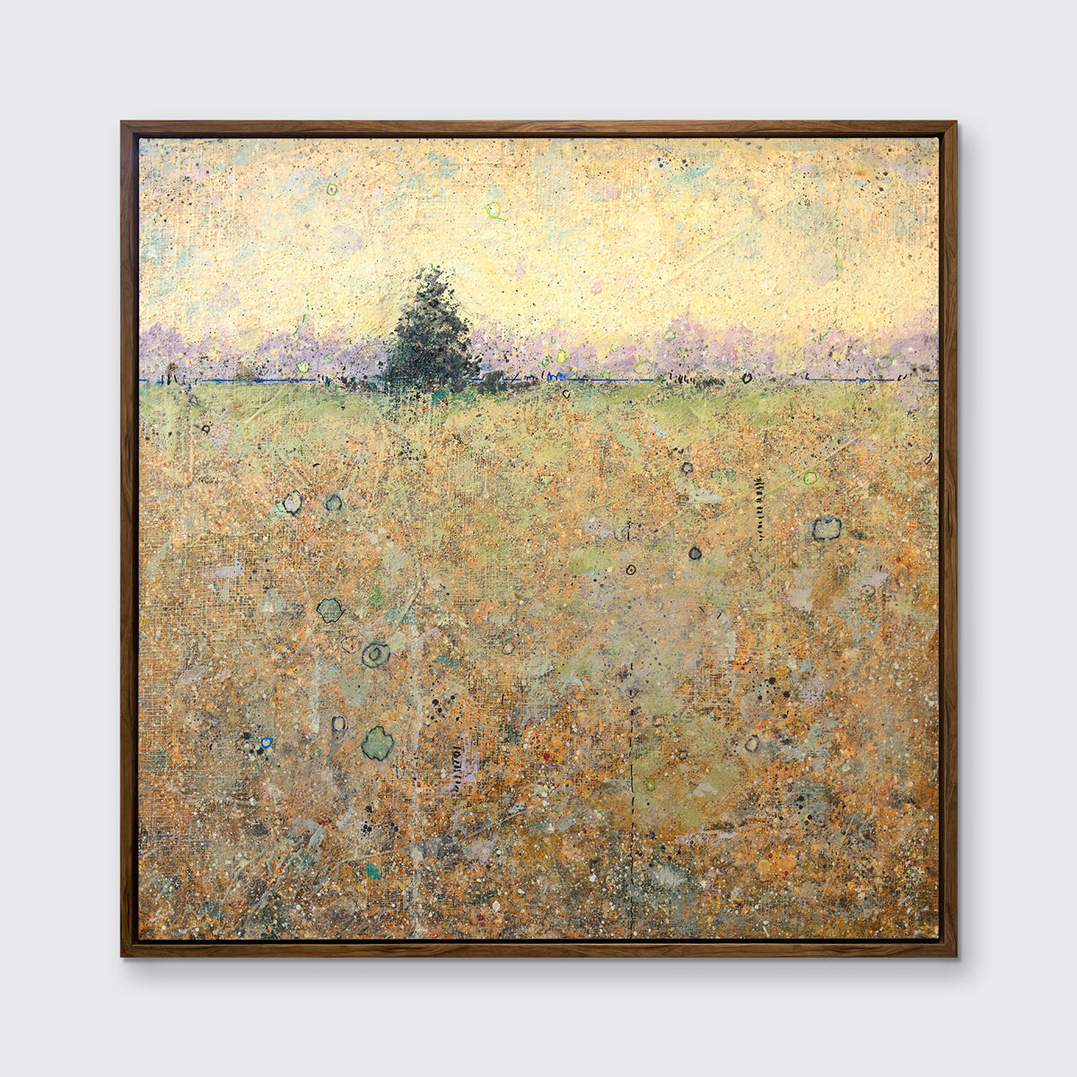 A yellow and green abstract landscape with a tree print in an oak wood floater frame hangs on a white wall.