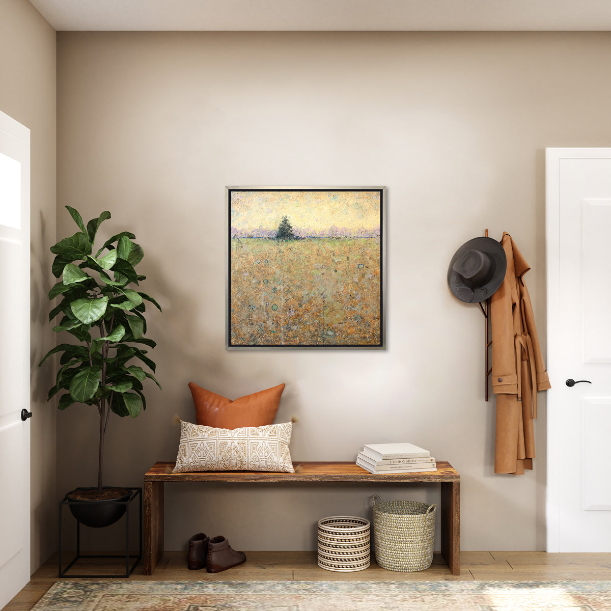 A green, orange and yellow abstract landscape print in a silver floater frame hangs on a white wall above a wood bench with pillows and a stack of books, a potted floor plant, a pair of brown ankle boots and two woven baskets.