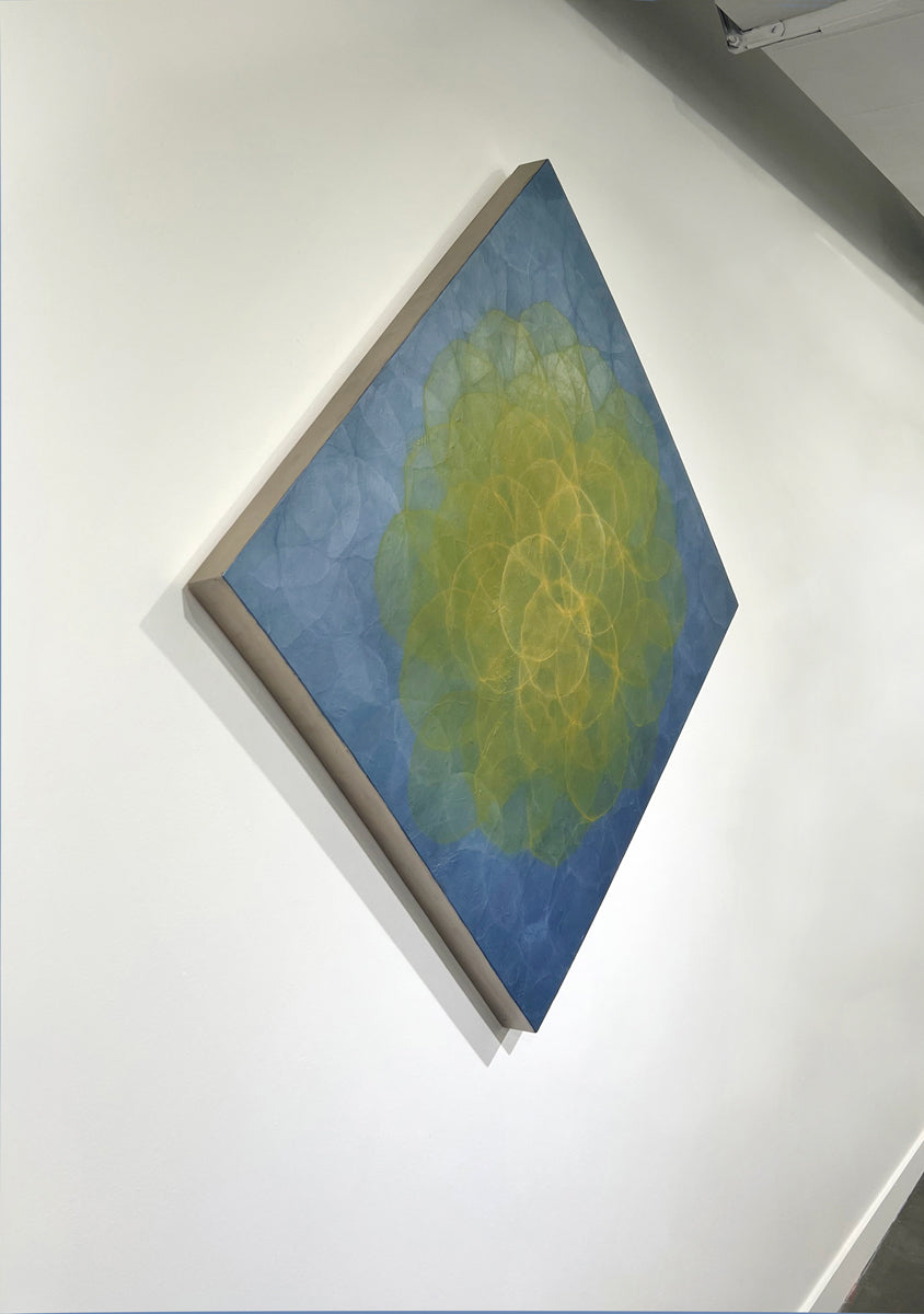 A blue and yellow abstract geometric painting hung on a white wall with a view from the left.