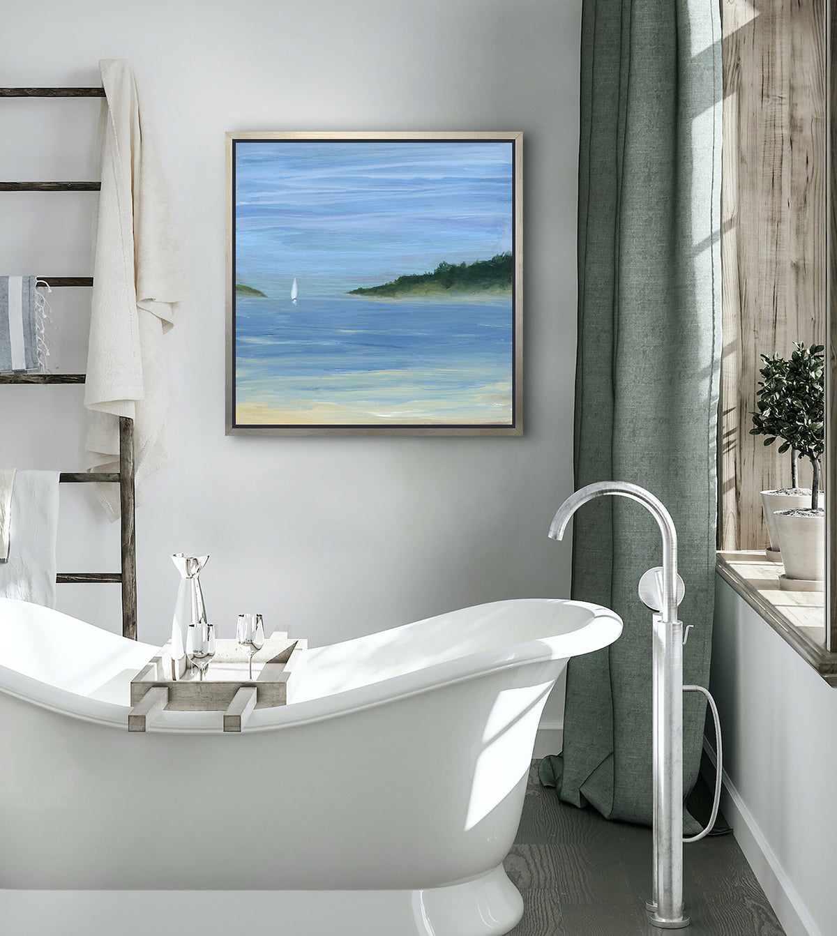 A blue, green and white abstract seascape print with a small sailboat in a silver floater frame hangs on a white wall above a modern white soaking bathtub, a ladder holding towels and a window sill with two potted toparies.