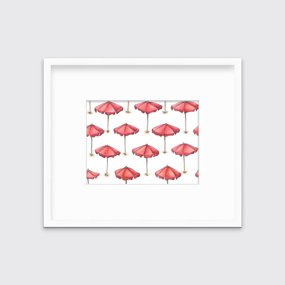 A print of red beach umbrellas with brown poles in a white frame with a mat hangs on a white wall.