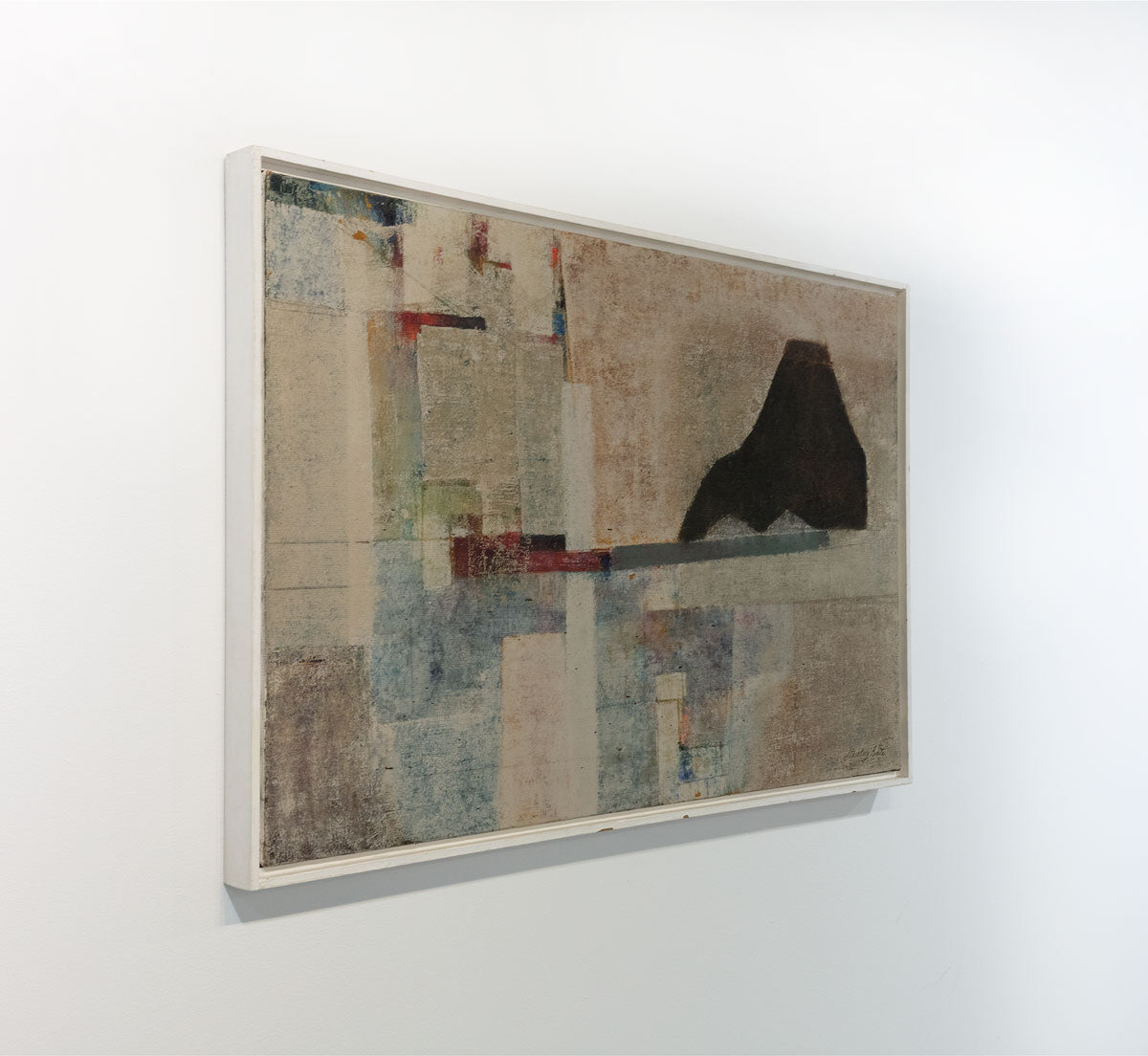An abstract painting by Stanley Bate adorned with textured geometric forms is seen from an angle. In the primary part of the composition a red and grey bar balances a black mountainous form.