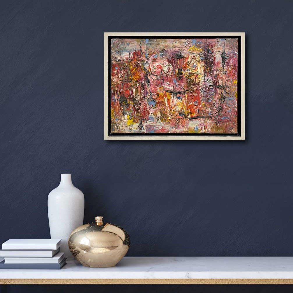 A multicolored abstract painting in a white floater frame hangs on a dark blue wall above a white marble console table with a white vase, a gold vase and a stack of four books.