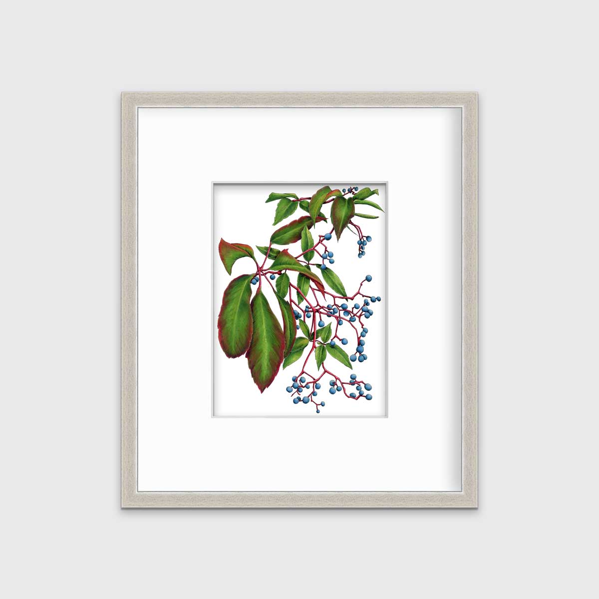 A green plant print with blue berries in a silver frame with a mat hangs on a white wall.