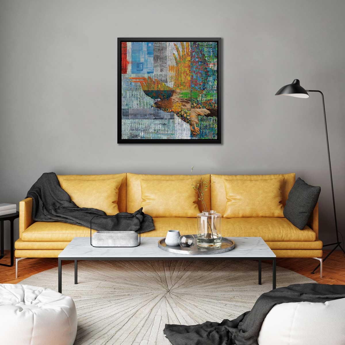 A multicolored abstract geometric print of a bald eagle in a black floater frame hangs on a grey wall above a dark yellow sofa with a black throw blanket, a white marble coffee table and two white bean bag chairs.