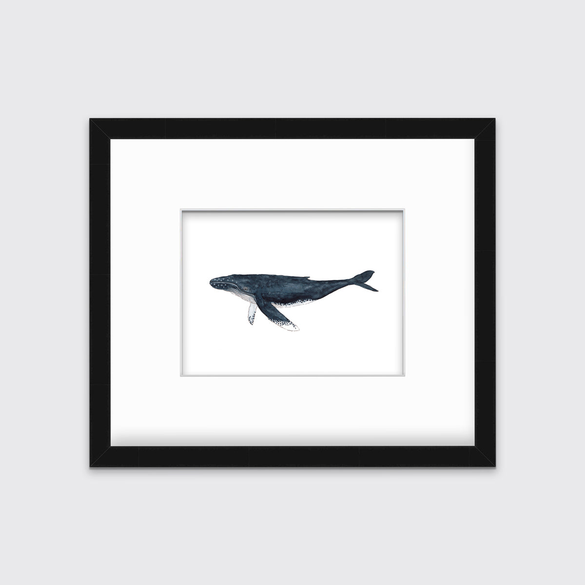 A blue and white whale print in a black frame with a mat hangs on a white wall.