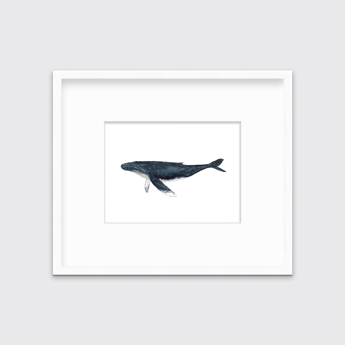 A blue and white whale print in a white frame with a mat hangs on a white wall.