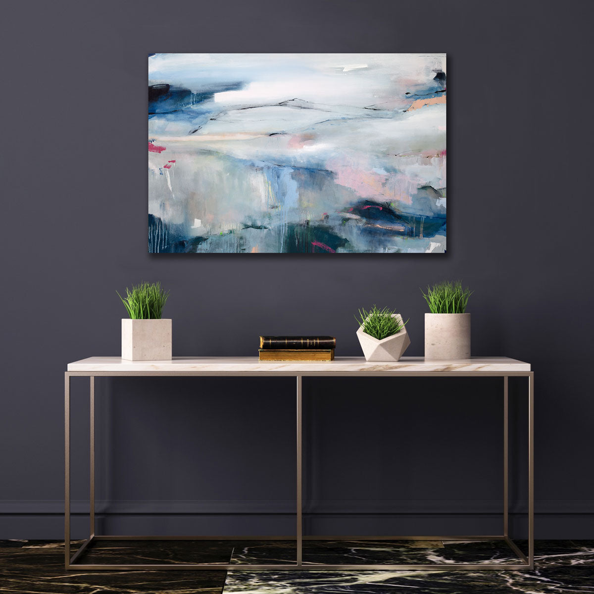 A blue abstract painting by Kelly Rossetti hangs on a dark grey wall above a white marble console table with small vases with greenery.