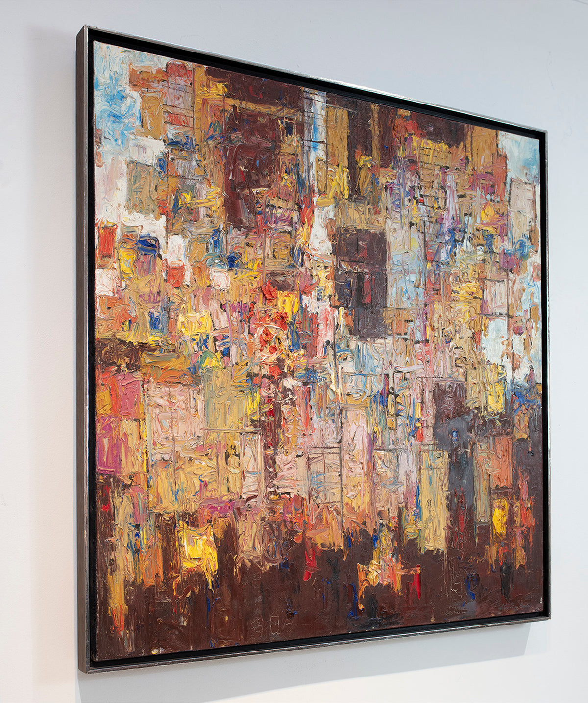 A left side-angle of a multicolored abstract painting in a silver frame hangs on a white wall.