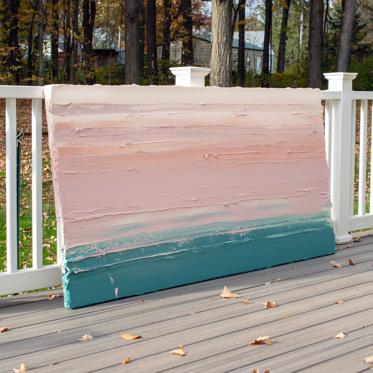 A peach, coral, pale pink and teal thick textured painting leaning outside on a deck in natural light of a painting by Teodora Guererra.