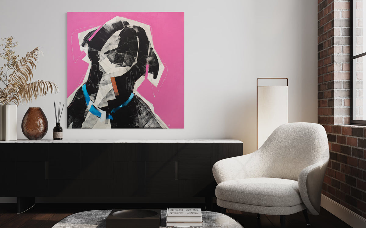 A large abstracted painting of a dog with a blue collar on a bright pink background hangs on a white wall above a large black and white console table with modern table decor, a coffee table, a floor lamp and a white armchair next to an exposed brick wall. 