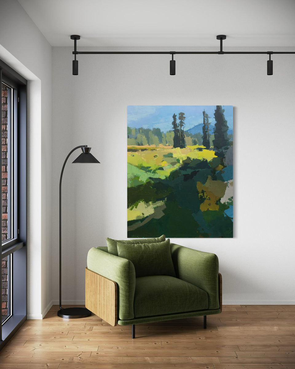 An abstracted blue and yellow painting hangs on a white wall next to a modern green armchair with black light stand to the side. 