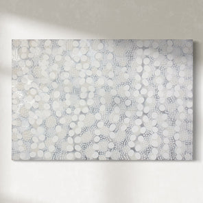 A white, grey, and silver abstract painting hangs on a sunny wall.