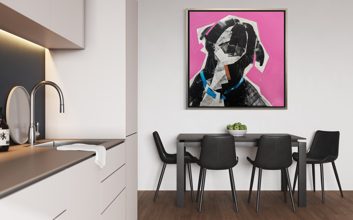 A pink, black, white and blue abstract dog print in a silver floater frame hangs on a white wall above a black table with a bowl of green apples and four black chairs surrounding.