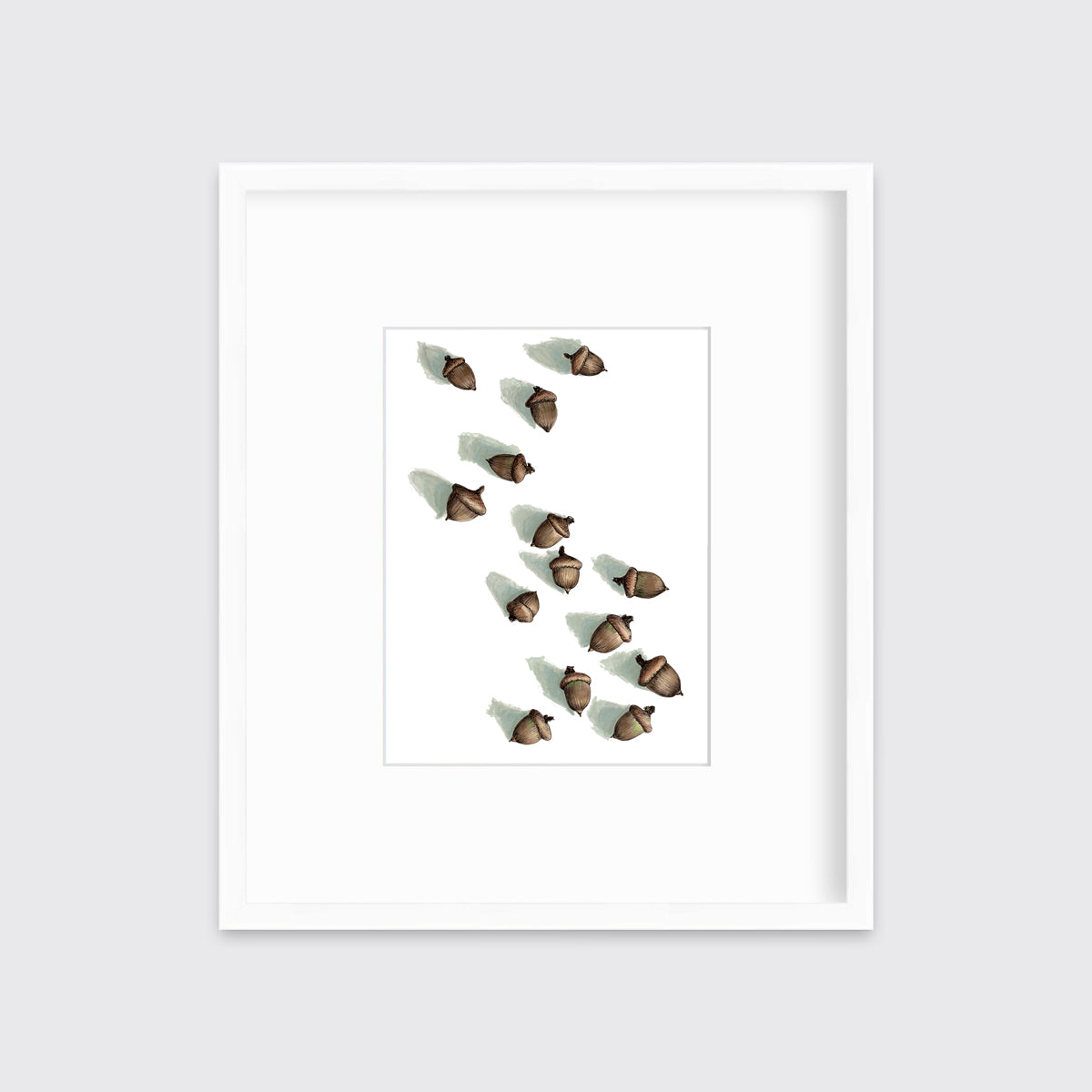 A print of several brown acorns with long shadows on a white background in a white frame with a mat hangs on a white wall.