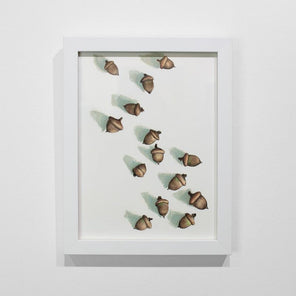 A framed illustration of acorns hangs on a white wall. 