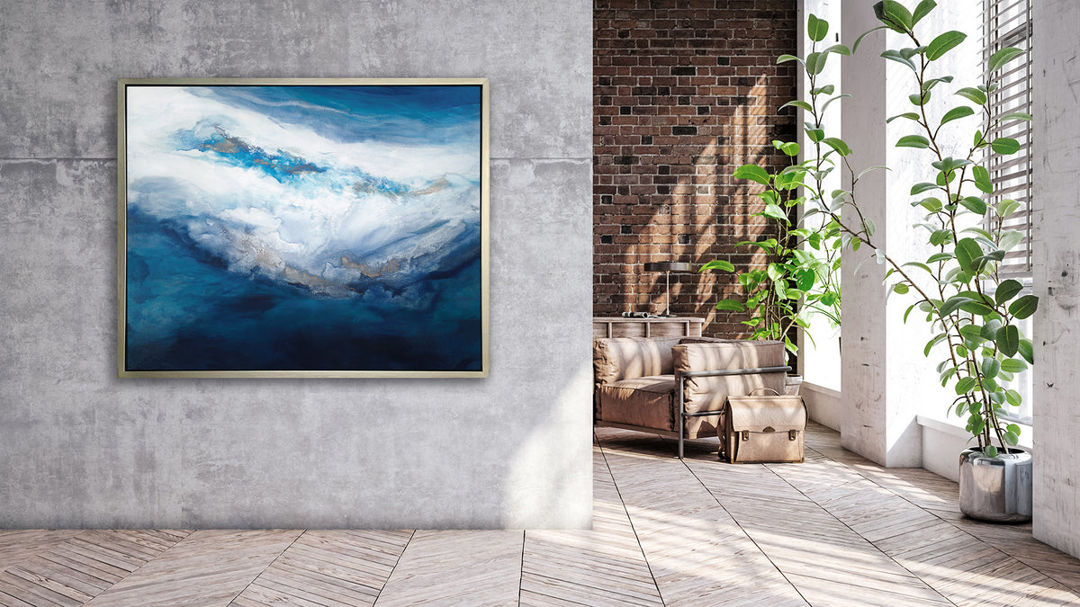 A blue, white, gold and teal abstract print in a silver floater frame hangs on a grey concrete wall next to an opening to a room with a brown leather chair, a briefcase and a tall potted floor plant.