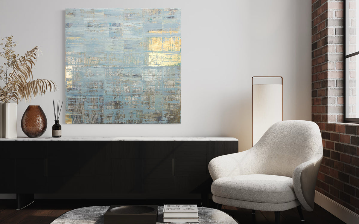 A blue and gold painting hangs on a white wall above a black and white console table with modern decor and a white suede armchair. 
